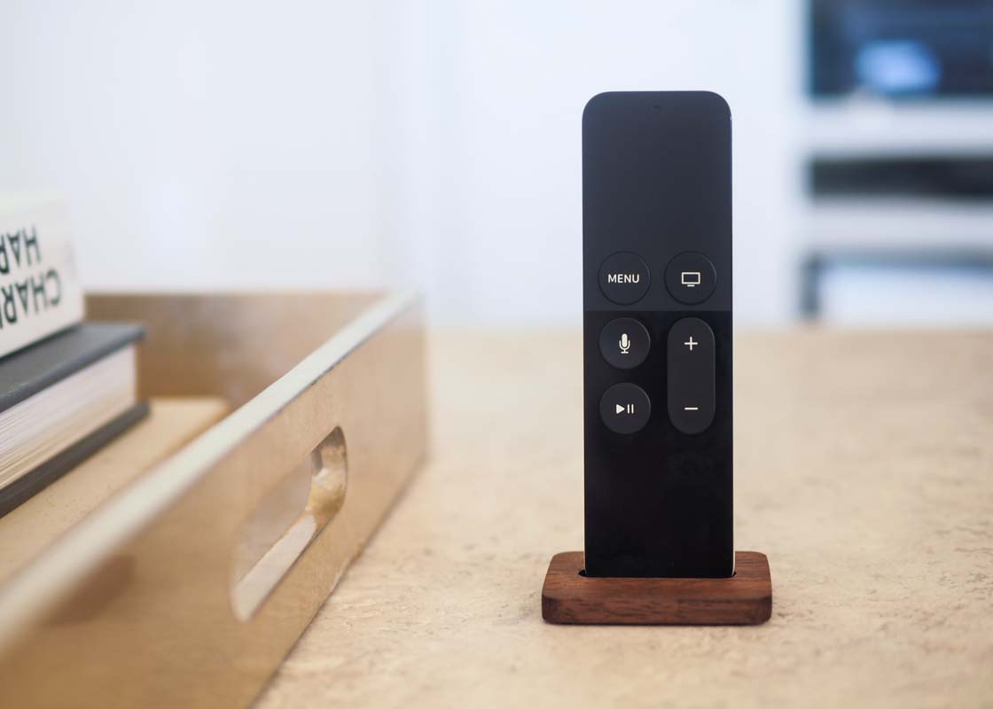 a close-up of the Apple TV remote on a stone coffee table being held upright by the stand.