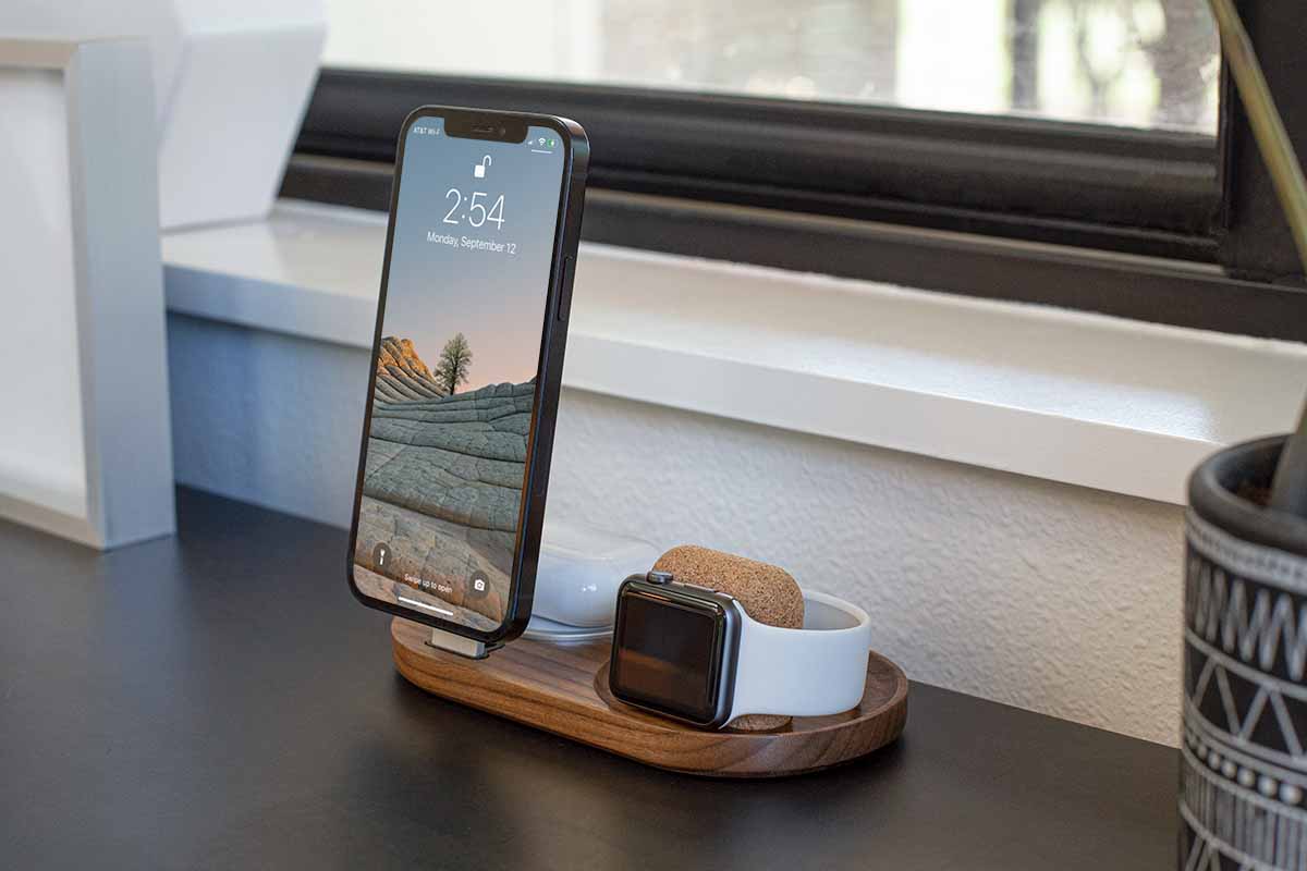 a phone laying on a qi charging pad, a phone standing upright charging via a lightning cable, and an Apple Watch charging on it's side, all on one dock.