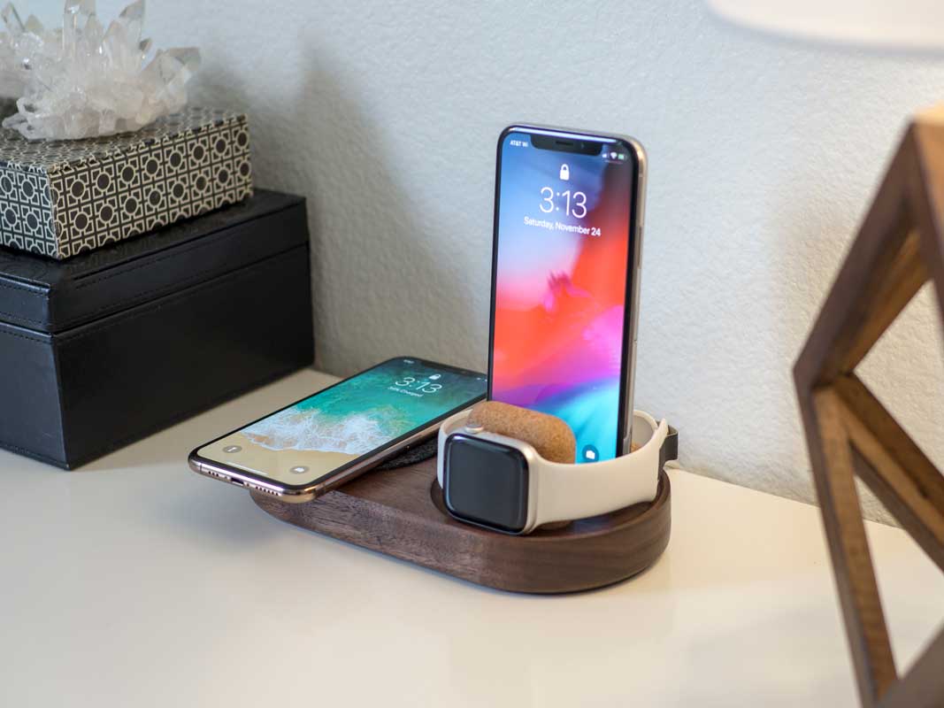 a phone laying on a qi charging pad, a phone standing upright charging via a lightning cable, and an Apple Watch charging on it's side, all on one dock.