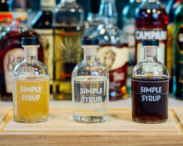 three different types of simple syrup in bottles on a cutting board.