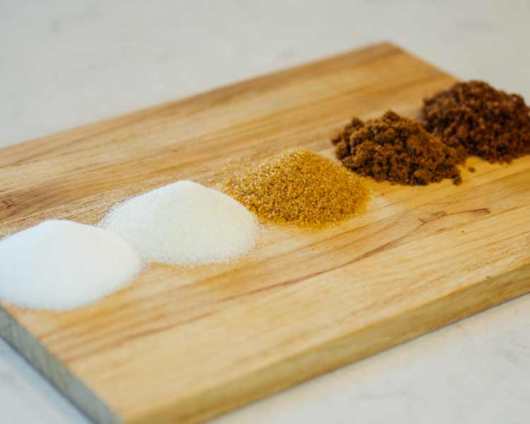 piles of different types of sugars on a cutting board.